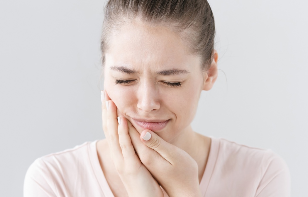Closeup of beautiful teenage girl isolated on gray background touching her face and closing eyes with expression of horrible suffer from health problem and aching tooth showing dissatisfaction.