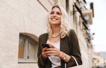 Image of caucasian woman wearing jacket using mobile phone for chat while walking through city street