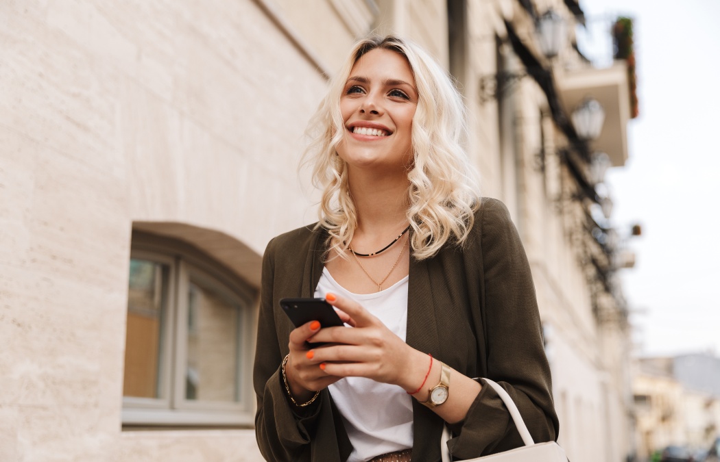 Image of caucasian woman wearing jacket using mobile phone for chat while walking through city street