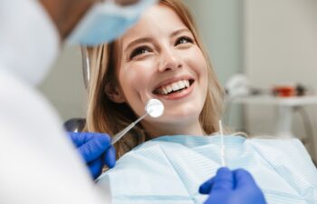 Image of pretty young woman sitting in dental chair at medical center while professional doctor fixing her teeth