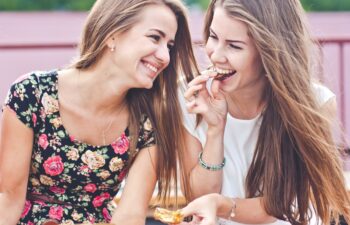 Two female friends have fun time outdoors in Russia, one girl bites chocolate and hands wrapper, another one just smiling, lifestyle shot