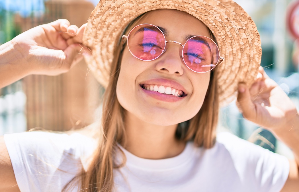 Young beautiful blonde caucasian woman smiling happy outdoors on a sunny day wearing summer hat and pink sunglasses