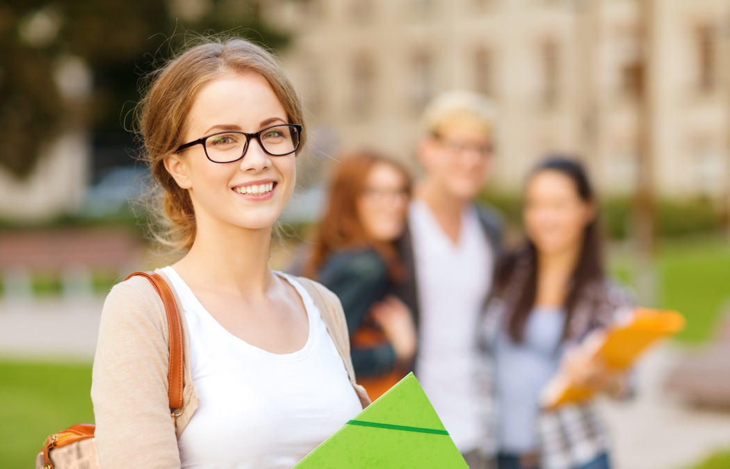 summer holidays, education, campus and teenage concept - smiling female student in black eyeglasses with folders and group in the back