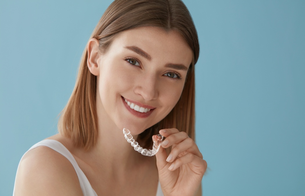 Teeth whitening. Woman with white smile, healthy straight teeth using clear removable braces, invisible teeth tray. Portrait of girl doing dental beauty treatment
