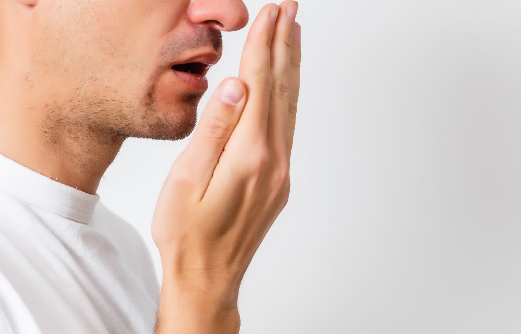 Bad breath. Halitosis concept. Young man checking his breath with his hand.