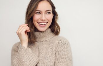 Portrait of young happy beautiful woman smiling and standing isolated on white background in a warm sweater. Young female girl with a perfect smile looking right.