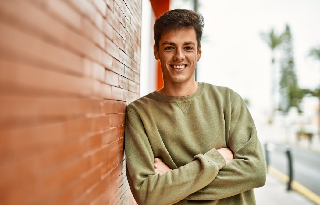 Young hispanic man smiling happy with arms crossed gesture at the city.