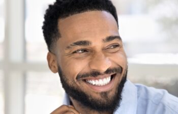 Cheerful attractive young Black man casual indoor portrait. Happy confident African professional, businessman, entrepreneur in office shirt looking away with perfect toothy smile